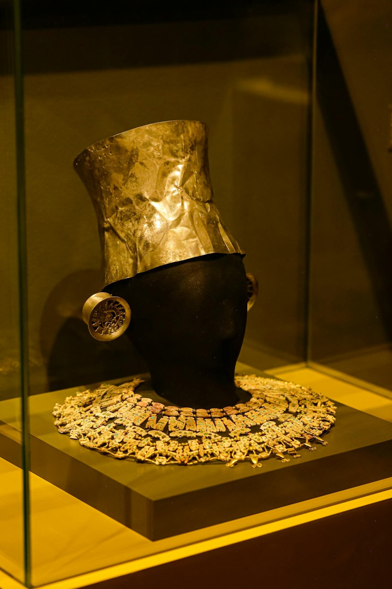 A museum exhibit showcasing ancient hat and elaborate jewelry in a glass case.