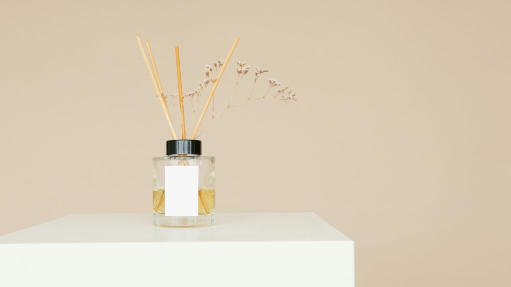 A minimalist reed diffuser with a mockup label on a white pedestal against a neutral background.